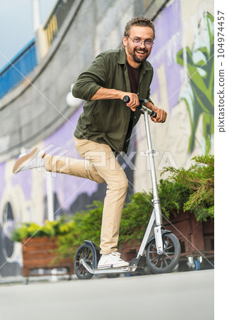 Happy and stylish metrosexual man riding a scooter on an urban background. With a joyful expression on his face, he embodies the spirit of fun and adventure as he glides through the city streets Happy and stylish metrosexual man riding a scooter on an urban background. With a joyful expression on his face, he embodies the spirit of fun and adventure as he glides through the city streets 104974457
