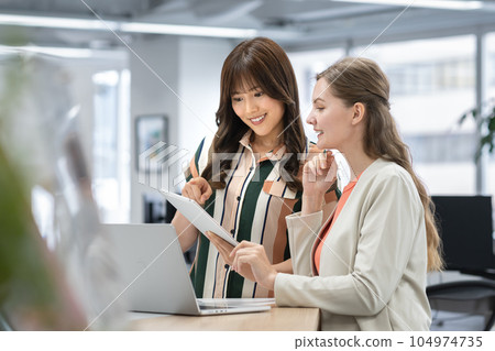 Global business image Japanese and foreign businesswomen talking in the office Global business image Japanese and foreign businesswomen talking in the office 104974735