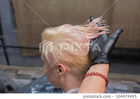 The hand of a girl of an experienced hairdresser in a black glove checks the degree of hair coloring, of an adult client in the salon The hand of a girl of an experienced hairdresser in a black glove checks the degree of hair coloring, of an adult client in the salon 104974995