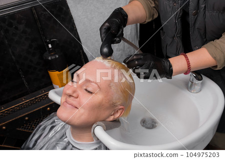 Satisfied adult attractive woman European customer barbershop in the process of washing hair with rain before cutting 104975203