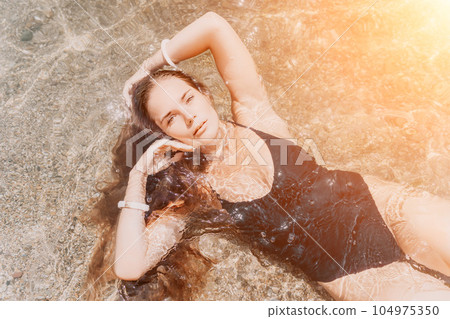 Woman summer travel sea. Happy tourist enjoy taking picture outdoors for memories. Woman traveler posing on the beach at sea surrounded by volcanic mountains, sharing travel adventure journey 104975350