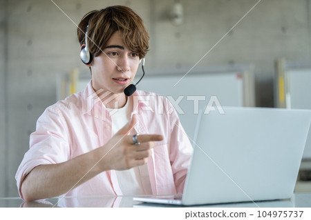 A young foreign man wearing a headset and talking into a computer A young foreign man wearing a headset and talking into a computer 104975737