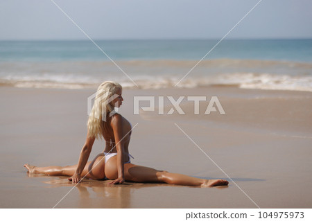 Tanned Bikini Beach Woman in Yoga Pose Doing Stretching Leg-split on Seashore Tanned Bikini Beach Woman in Yoga Pose Doing Stretching Leg-split on Seashore 104975973