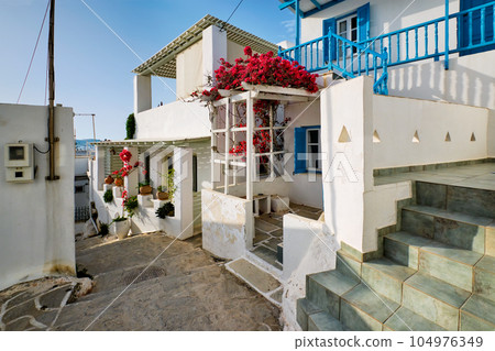 Picturesque narrow street with traditional whitewashed houses with blooming bougainvillea flowers of Naousa town in famous tourist attraction Paros island, Greece 104976349