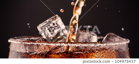 Pouring of Cola and Ice. Cola soda and ice splashing fizzing or floating up to top of surface. Close up of ice in cola water. Texture of carbonate drink with bubbles in glass. Cold drink background Pouring of Cola and Ice. Cola soda and ice splashing fizzing or floating up to top of surface. Close up of ice in cola water. Texture of carbonate drink with bubbles in glass. Cold drink background 104978437
