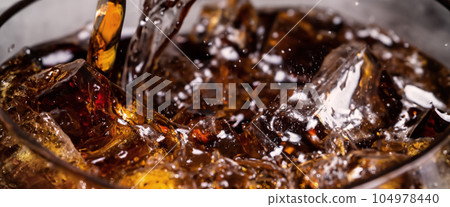 Pouring of Cola and Ice. Cola soda and ice splashing fizzing or floating up to top of surface. Close up of ice in cola water. Texture of carbonate drink with bubbles in glass. Cold drink background Pouring of Cola and Ice. Cola soda and ice splashing fizzing or floating up to top of surface. Close up of ice in cola water. Texture of carbonate drink with bubbles in glass. Cold drink background 104978440