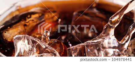 Pouring of Cola and Ice. Cola soda and ice splashing fizzing or floating up to top of surface. Close up of ice in cola water. Texture of carbonate drink with bubbles in glass. Cold drink background Pouring of Cola and Ice. Cola soda and ice splashing fizzing or floating up to top of surface. Close up of ice in cola water. Texture of carbonate drink with bubbles in glass. Cold drink background 104978441