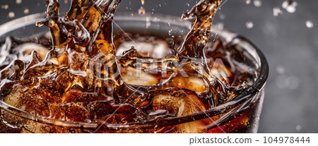 Pouring of Cola and Ice. Cola soda and ice splashing fizzing or floating up to top of surface. Close up of ice in cola water. Texture of carbonate drink with bubbles in glass. Cold drink background 104978444