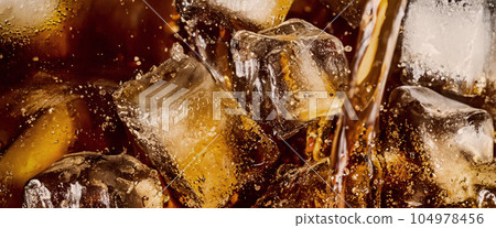 Pouring of Cola and Ice. Cola soda and ice splashing fizzing or floating up to top of surface. Close up of ice in cola water. Texture of carbonate drink with bubbles in glass. Cold drink background 104978456