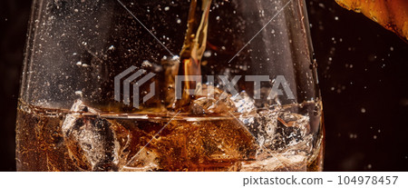 Pouring of Cola and Ice. Cola soda and ice splashing fizzing or floating up to top of surface. Close up of ice in cola water. Texture of carbonate drink with bubbles in glass. Cold drink background Pouring of Cola and Ice. Cola soda and ice splashing fizzing or floating up to top of surface. Close up of ice in cola water. Texture of carbonate drink with bubbles in glass. Cold drink background 104978457