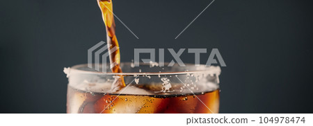 Pouring of Cola and Ice. Cola soda and ice splashing fizzing or floating up to top of surface. Close up of ice in cola water. Texture of carbonate drink with bubbles in glass. Cold drink background 104978474