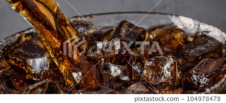 Pouring of Cola and Ice. Cola soda and ice splashing fizzing or floating up to top of surface. Close up of ice in cola water. Texture of carbonate drink with bubbles in glass. Cold drink background Pouring of Cola and Ice. Cola soda and ice splashing fizzing or floating up to top of surface. Close up of ice in cola water. Texture of carbonate drink with bubbles in glass. Cold drink background 104978478