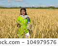 Girl waving flag of Pakistan outdoors over blue cloudy sky and golden wheat. 104979576