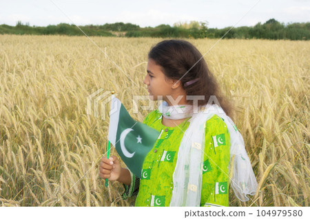Girl waving flag of Pakistan outdoors over blue cloudy sky and golden wheat. 104979580