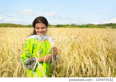 Cute pakistani girl in national dress stends in the field of golden wheat and smiling Cute pakistani girl in national dress stends in the field of golden wheat and smiling 104979582