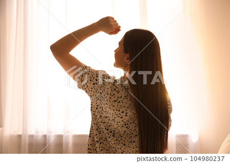 Young woman stretching near window at home. Lazy morning 104980237