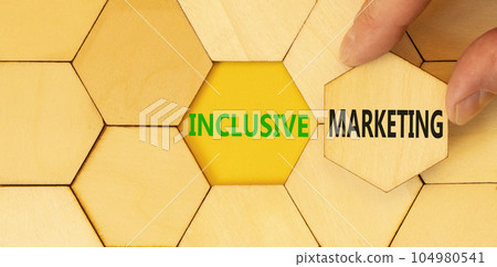 Inclusive marketing symbol. Concept words Inclusive marketing on beautiful wooden puzzles. Beautiful yellow background. Businessman hand. Business inclusive marketing concept. Copy space. Inclusive marketing symbol. Concept words Inclusive marketing on beautiful wooden puzzles. Beautiful yellow background. Businessman hand. Business inclusive marketing concept. Copy space. 104980541