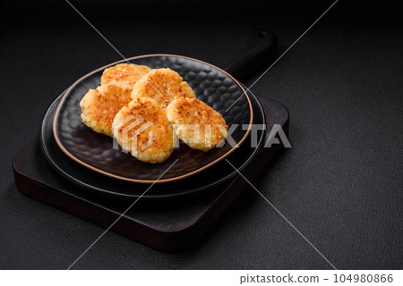 Delicious fresh cottage cheesecakes with raisins and vanilla on a black ceramic plate Delicious fresh cottage cheesecakes with raisins and vanilla on a black ceramic plate 104980866