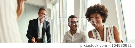 Great results Group of young business people looking at documents and smiling while sitting at the office table 104980951