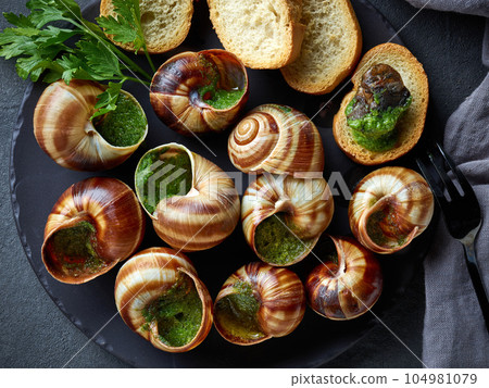 plate of baked escargot snails filled with parsley and garlic butter 104981079