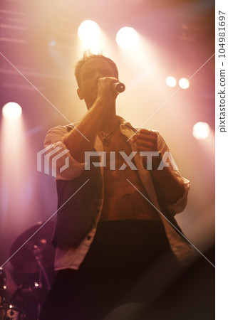 Concert, music and singer with man on stage for night, festival and rock performance. Spotlight, karaoke and band with male artist singing in show for musician, clubbing and disco party event 104981697