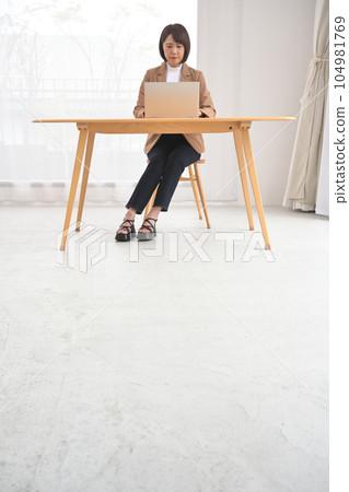 Woman working on a laptop at a wooden desk indoors 104981769
