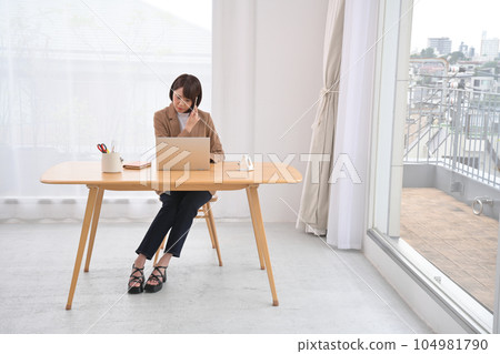 Woman calling with laptop and smartphone at wooden desk indoors Woman calling with laptop and smartphone at wooden desk indoors 104981790