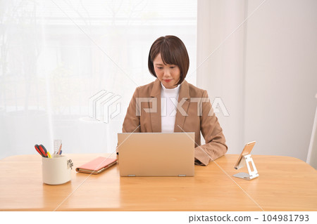 Woman working on a laptop at a wooden desk indoors Woman working on a laptop at a wooden desk indoors 104981793