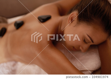 Back, hot stone massage and woman in bed with luxury service for muscle, body and relax with peace in resort. Girl, hospitality and physical therapy for spine with wellness, spa and natural healing 104981974