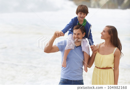 Family, summer and walking outdoor at beach for travel holiday with a smile and fun. A man, woman and child or son on shoulders while playing together on vacation at sea with happiness, love and care 104982168