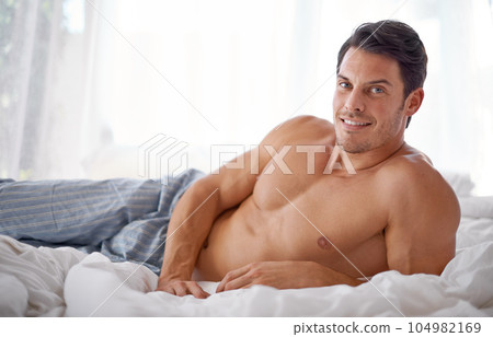 Sexy, smile and portrait of a man on a bed for relaxing, comfort and rest in pyjamas. Comfy, cozy and handsome young man content in the bedroom, smiling and confident to relax on the weekend 104982169