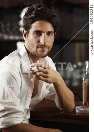 Portrait, young man and smoking at a bar or cigarette at hand or handsome guy relaxing and unbuttoned shirt. Sexy, masculine and attractive model with ash tray or about to have a drink after work 104982218
