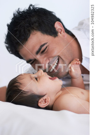 Baby, laugh and dad on a bedroom bed with happiness, bonding and parent care with smile. Father, happy and young child together in a home playing and kid laughing from papa love and youth support 104982325
