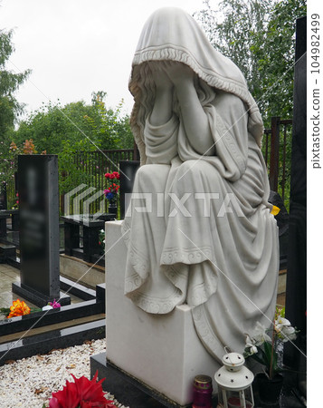 Weeping woman. Sculpture in the cemetery. The figure of a mother, wife or woman in a hood or stole. Lamentation for the deceased. Tombstone on a Christian grave. Sadness and grief Weeping woman. Sculpture in the cemetery. The figure of a mother, wife or woman in a hood or stole. Lamentation for the deceased. Tombstone on a Christian grave. Sadness and grief 104982499