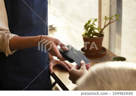 Hand, credit card and pos terminal in a coffee shop for payment by a customer to a waitress for service. Finance, bill and nfc with a person paying using wireless technology in a cafe or restaurant Hand, credit card and pos terminal in a coffee shop for payment by a customer to a waitress for service. Finance, bill and nfc with a person paying using wireless technology in a cafe or restaurant 104982689