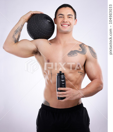 Remember to keep hydrated. a male athlete holding a medicine ball and water bottle against a studio background. Remember to keep hydrated. a male athlete holding a medicine ball and water bottle against a studio background. 104983033