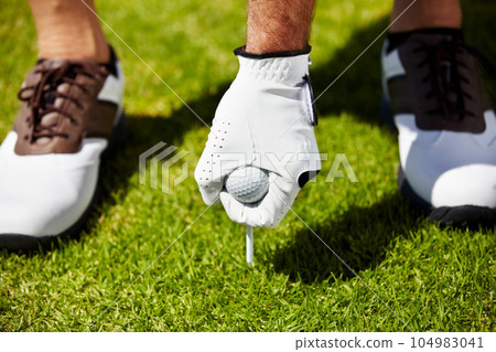 Golf ball, tee and hands of man on grass field for contest, competition challenge and sports target on course. Closeup, lawn and golfer gloves with pin in ground for action, games and training gear Golf ball, tee and hands of man on grass field for contest, competition challenge and sports target on course. Closeup, lawn and golfer gloves with pin in ground for action, games and training gear 104983041