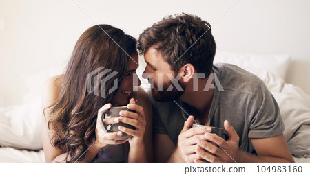 Relax, coffee and love with couple in bedroom for morning, wake up and affectionate. Happy, smile and free time with man and woman and kiss in bed at home for weekend, happiness and romance together 104983160