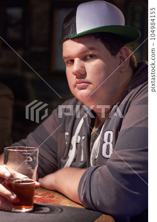 Man portrait, pub beer and plus size person waiting for a alcohol and drink looking serious. Male person, restaurant and glass pint sitting at a counter at a club with gen z, cool and urban fashion Man portrait, pub beer and plus size person waiting for a alcohol and drink looking serious. Male person, restaurant and glass pint sitting at a counter at a club with gen z, cool and urban fashion 104984155