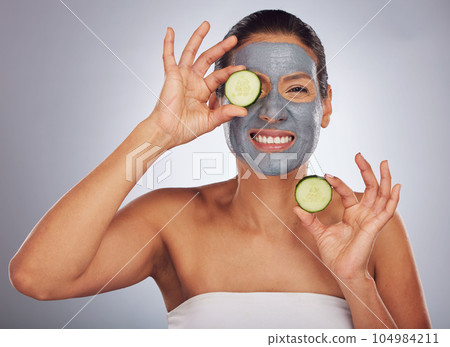 Portrait, cucumber and mask with a model woman in studio on a gray background for an antiaging facial treatment. Beauty, skincare and fruit with a young female person using cosmetic lay on her face 104984211