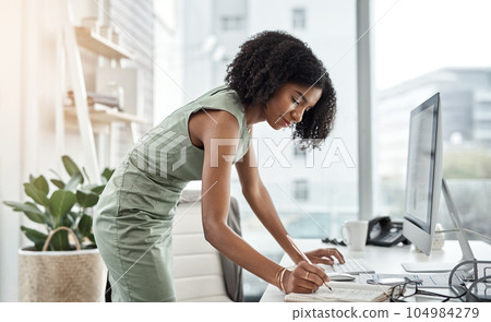 Computer, schedule and business woman writing and standing by her desk or table in a corporate startup. Internet, online and professional female employee, assistant or planner planning in a notebook 104984279