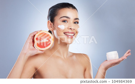 Skincare, face cream and woman with grapefruit in studio for a natural, organic or health facial routine. Beauty, self care and female model with citrus fruit and spf for treatment by gray background Skincare, face cream and woman with grapefruit in studio for a natural, organic or health facial routine. Beauty, self care and female model with citrus fruit and spf for treatment by gray background 104984369