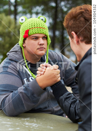 Arm wrestling, friends and outdoor at table for sports, challenge and exercise. Strong, conflict and men holding hands for competition, serious power and muscle match, training or workout in park. Arm wrestling, friends and outdoor at table for sports, challenge and exercise. Strong, conflict and men holding hands for competition, serious power and muscle match, training or workout in park. 104984382