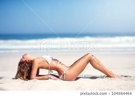 Woman on beach sand, model in bikini and body in sexy pose, nature and travel with summer fashion on vacation. Female person relax, sun and sea with sunbathing outdoor and holiday in stylish swimsuit 104984464