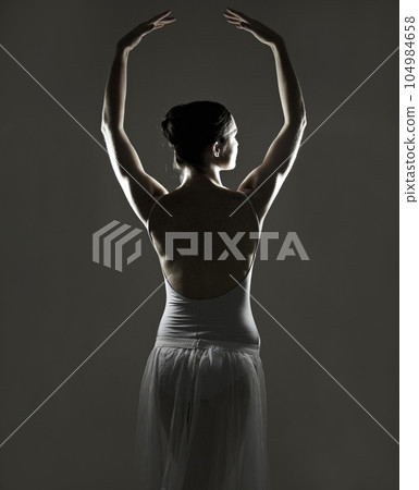 Art, silhouette and back of a ballet dancer in a studio with elegant posture, pose or position. Creative, monochrome and female ballerina doing a classical dance or performance by a black background. Art, silhouette and back of a ballet dancer in a studio with elegant posture, pose or position. Creative, monochrome and female ballerina doing a classical dance or performance by a black background. 104984658