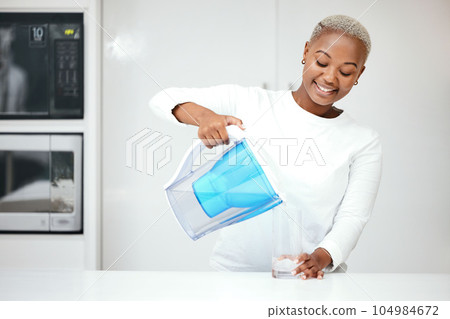 Water, filter and black woman with jug in kitchen to refresh with glass, liquid and cold hydration. Happy, thirsty and female person pouring pure aqua beverage from pitcher for clean drinking at home 104984672