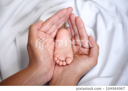 Hands, newborn and closeup of a baby foot with mother holding for care, love and nurture. Childcare, cute and zoom of a woman with her infant child feet in the crib of nursery at their family home. Hands, newborn and closeup of a baby foot with mother holding for care, love and nurture. Childcare, cute and zoom of a woman with her infant child feet in the crib of nursery at their family home. 104984967