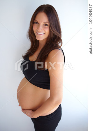 Woman, pregnancy portrait and stomach by wall with smile, excited or pride for new life, future or family. Young mom, pregnant and holding belly with happiness, love or care in house with expectation Woman, pregnancy portrait and stomach by wall with smile, excited or pride for new life, future or family. Young mom, pregnant and holding belly with happiness, love or care in house with expectation 104984987