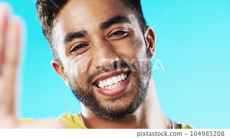 Selfie, laughing and face of a man with a smile isolated on a blue background in a studio. Happy, cheerful and portrait of a young guy taking a photo, smiling and posing for a picture on a backdrop 104985208