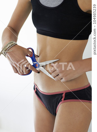 Scissors, stomach and woman with anorexia in studio for mental health, crisis or problem on white background. Weight loss, cutting and slimming female with body dysmorphia, bulimia or eating disorder 104985239